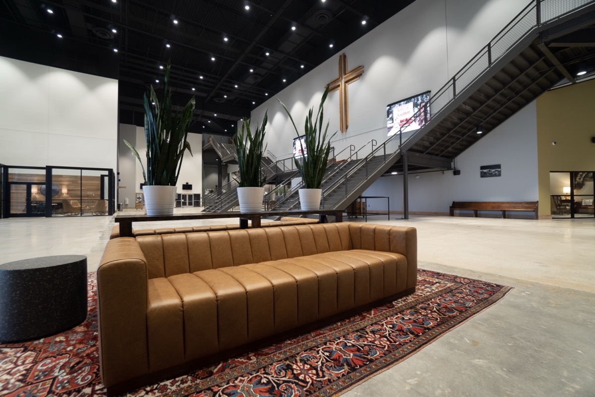 Warm church lobby with a leather couch, plants, and a cross on the wall behind